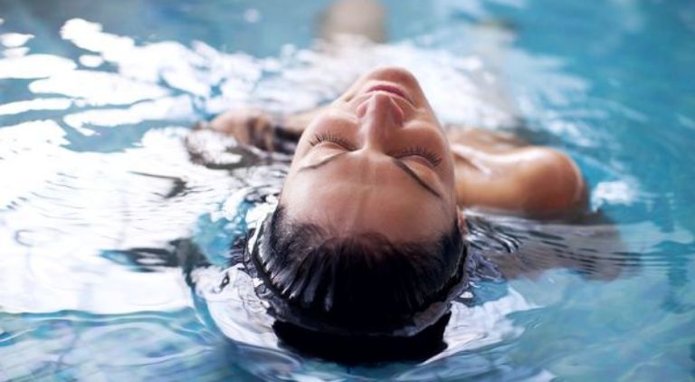woman lying relaxed on her back in the pool with her head sticking out