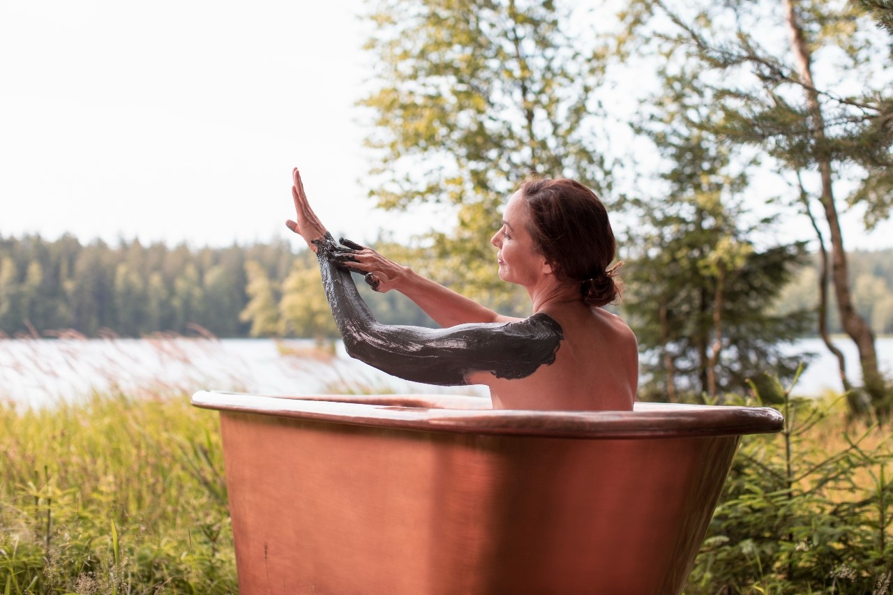 A woman rubbing herself with healing mud in a bathtub in nature